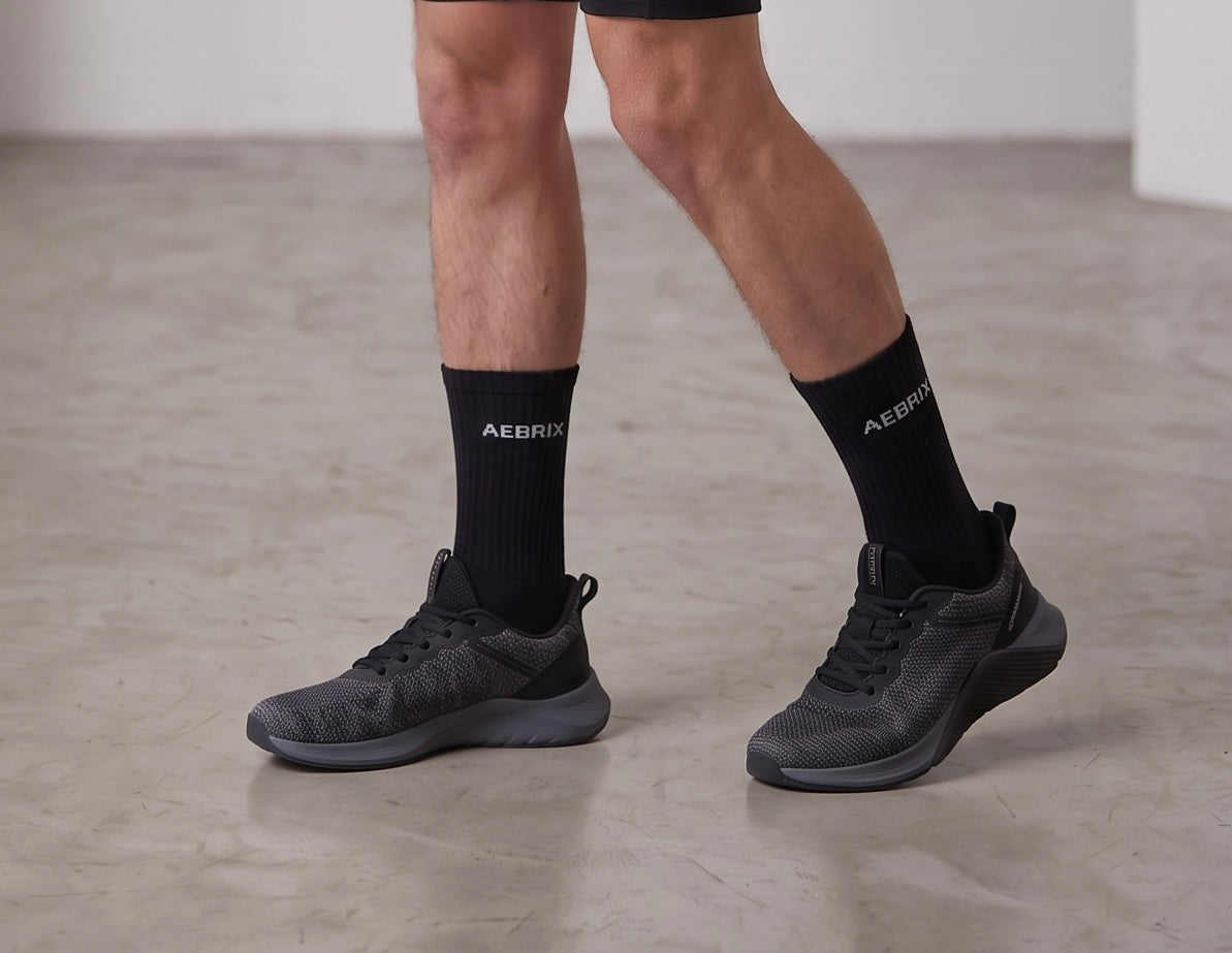 A person wearing black athletic socks with the brand name 'AEBIT' and black sneakers, shown from the knees down on a concrete floor.