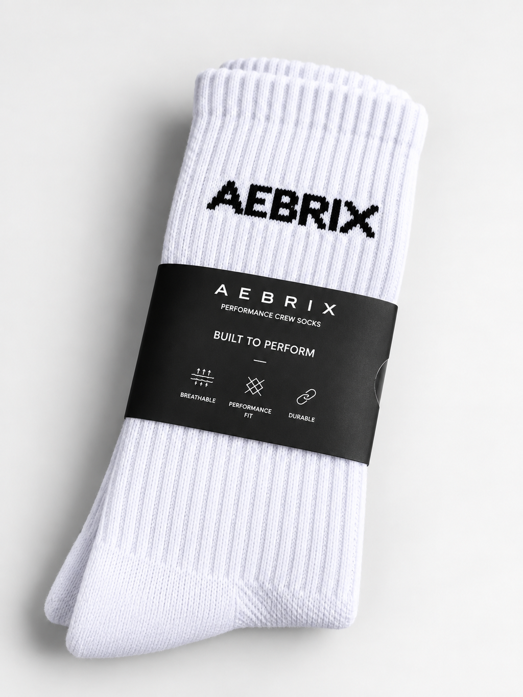 A pair of white ribbed crew socks with the brand name 'AEBRIX' printed in black near the cuff, wrapped in a black paper band that reads 'AEBRIX PERFORMANCE CREW SOCKS'.