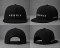 A black snapback cap shown from four angles in a 2x2 grid. The front and side views show the brand name 'AEBRIX' in white text, while the back views show the adjustable strap closure.